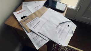 Energy, car insurance and council tax post piled on a hallway table with a phone on top, illustrating cashback on bills