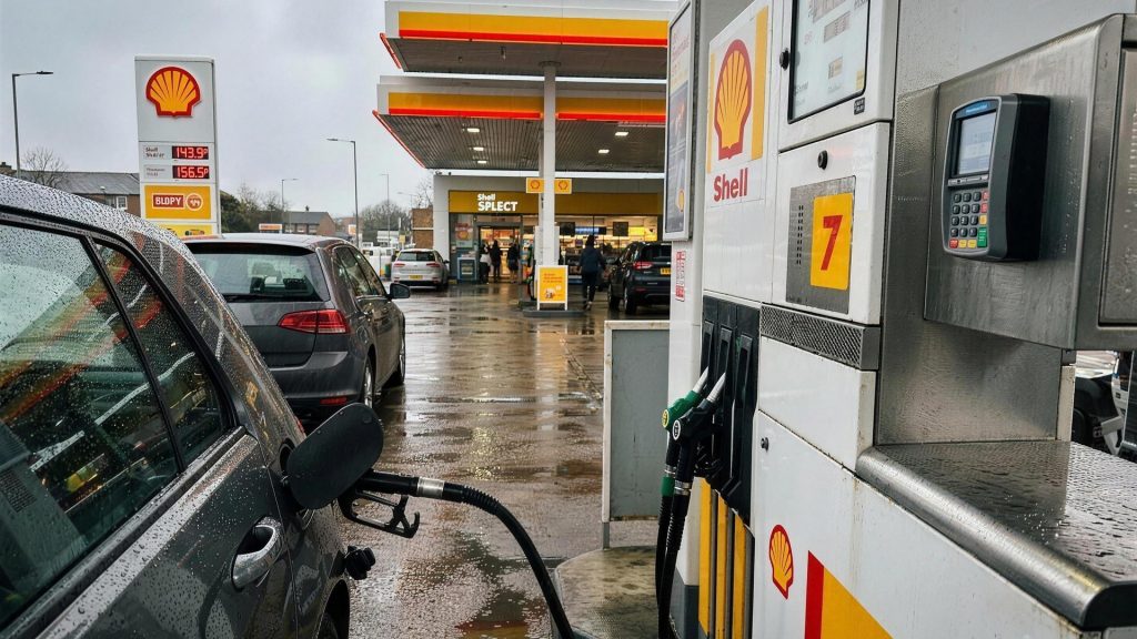 Contactless bank card being used at a Shell fuel pump on a wet UK forecourt, illustrating cashback on fuel