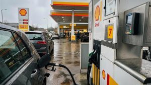 Contactless bank card being used at a Shell fuel pump on a wet UK forecourt, illustrating cashback on fuel