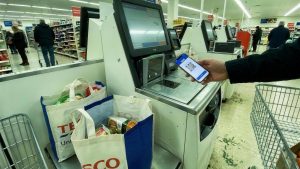 Shopper scanning a digital gift card QR code on a phone at a Tesco self-checkout, illustrating supermarket cashback on a food shop